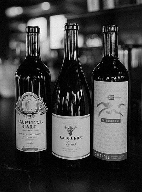 Thee bottles of wine on bar top including Capital Call Cabernet Sauvignon, La Bruere Syrah, Windhorse and Zinfandel.