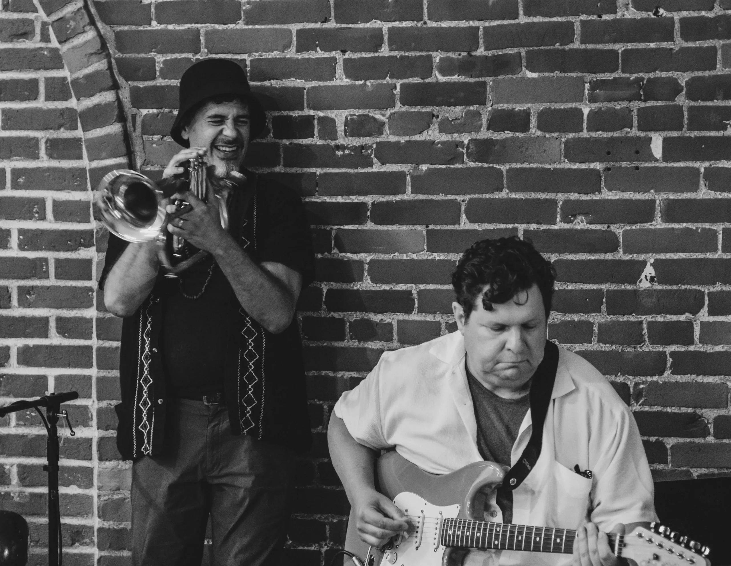 A musician on the trumpet and one on the guitar. Black and white.